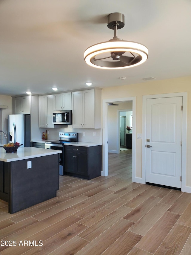 kitchen featuring white cabinets, light hardwood / wood-style flooring, pendant lighting, and stainless steel appliances