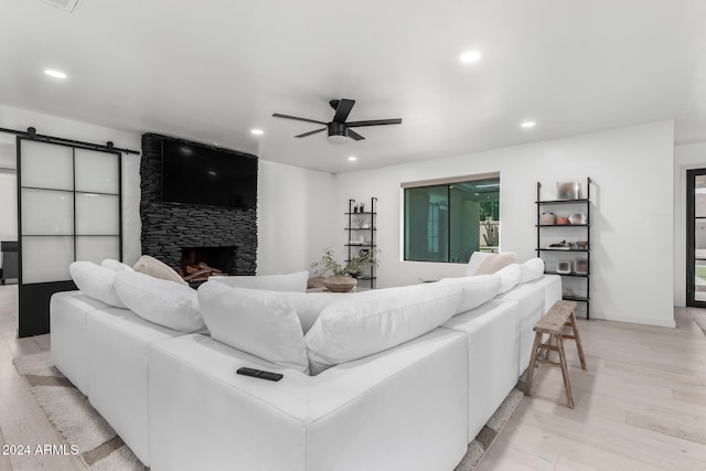 living room with light wood-type flooring, a barn door, ceiling fan, and a fireplace