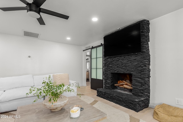 living room with light hardwood / wood-style flooring, a barn door, ceiling fan, and a fireplace