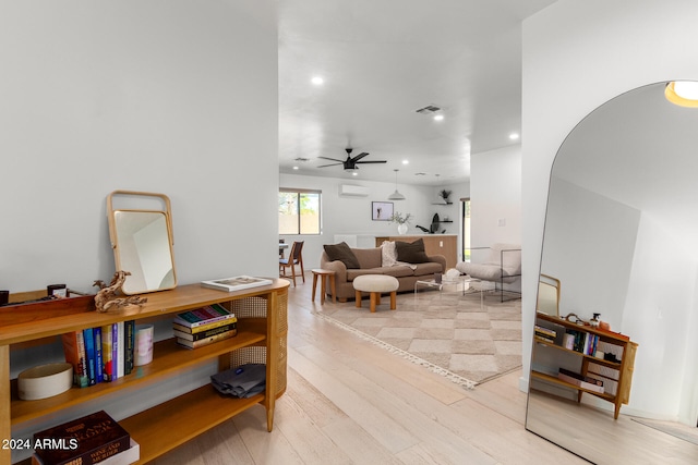 living room featuring a wall mounted AC, light hardwood / wood-style flooring, and ceiling fan