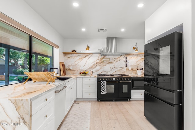 kitchen with black appliances, white cabinetry, sink, wall chimney exhaust hood, and light hardwood / wood-style flooring