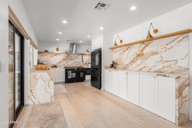 kitchen with wall chimney exhaust hood, black appliances, backsplash, white cabinetry, and light wood-type flooring