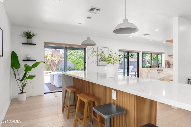 kitchen featuring decorative light fixtures, a kitchen bar, a healthy amount of sunlight, and light hardwood / wood-style flooring