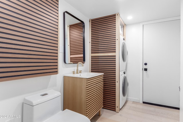 bathroom featuring stacked washing maching and dryer, vanity, hardwood / wood-style flooring, and toilet