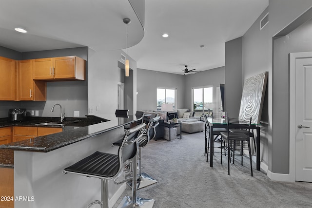 kitchen featuring decorative light fixtures, ceiling fan, dark stone countertops, light carpet, and sink