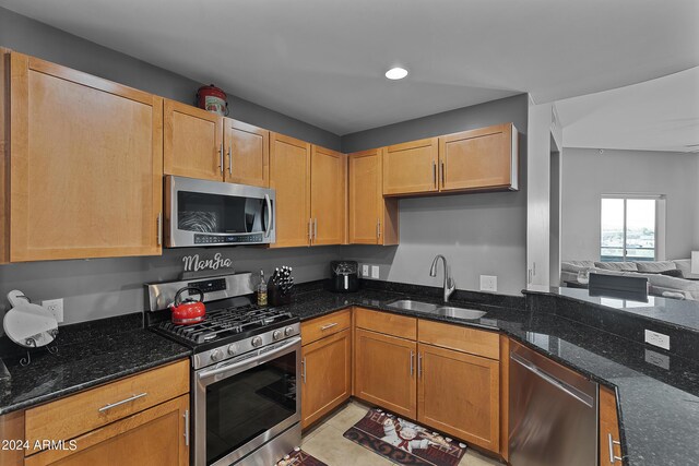 kitchen with appliances with stainless steel finishes, sink, dark stone countertops, and light tile floors