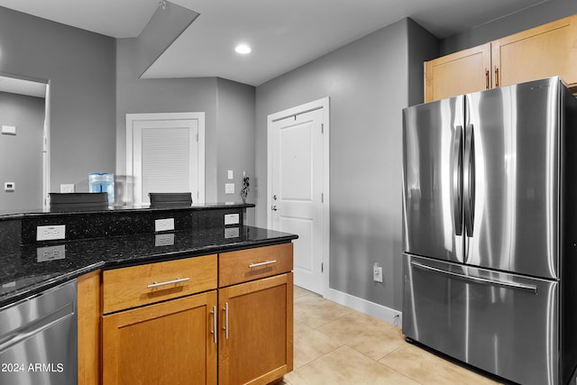 kitchen with dark stone counters, stainless steel fridge, and light tile floors