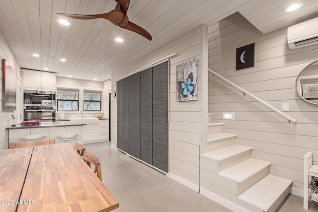 kitchen featuring wood ceiling, an AC wall unit, double oven, ceiling fan, and white cabinets