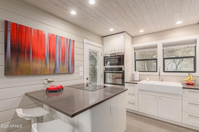 kitchen with sink, a breakfast bar area, wooden walls, white cabinets, and black electric cooktop