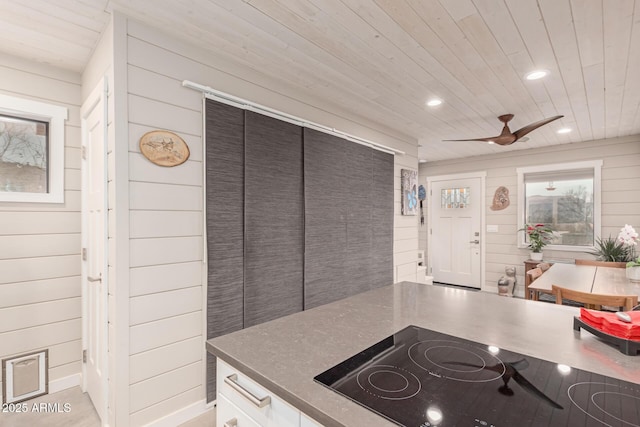 kitchen with black electric cooktop, wooden ceiling, ceiling fan, and wood walls