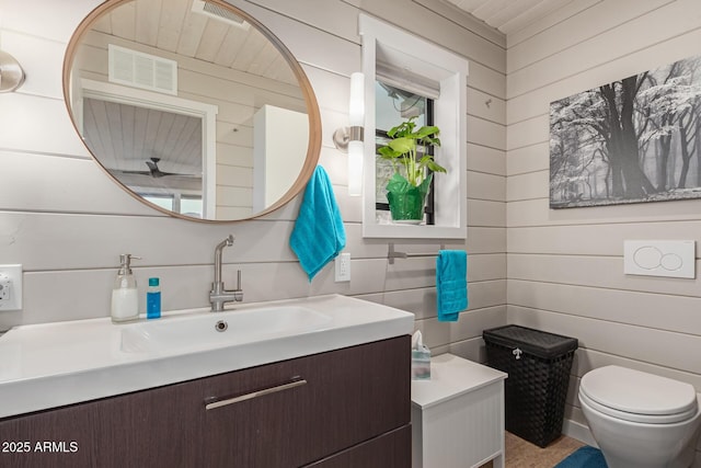 bathroom with vanity, wooden walls, and toilet