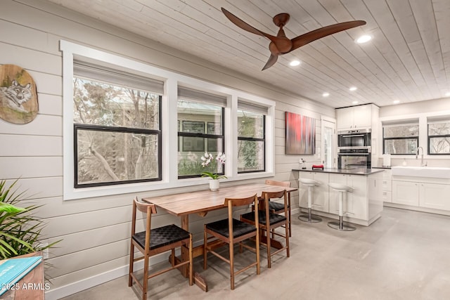 dining room featuring sink, ceiling fan, wooden walls, breakfast area, and wooden ceiling