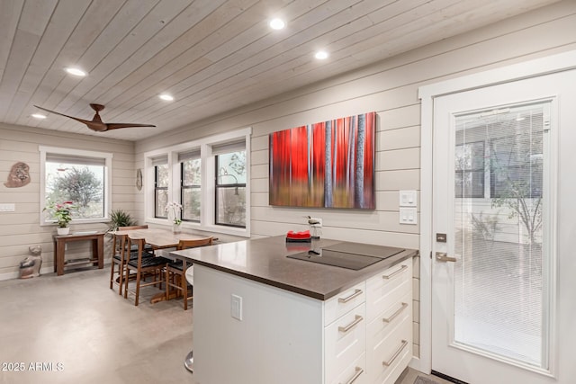 kitchen with wood walls, wooden ceiling, ceiling fan, black electric stovetop, and white cabinets