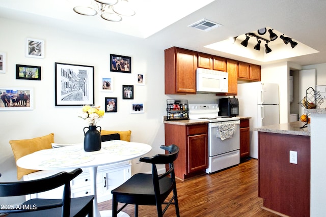 kitchen featuring visible vents, white appliances, dark wood finished floors, a tray ceiling, and brown cabinetry