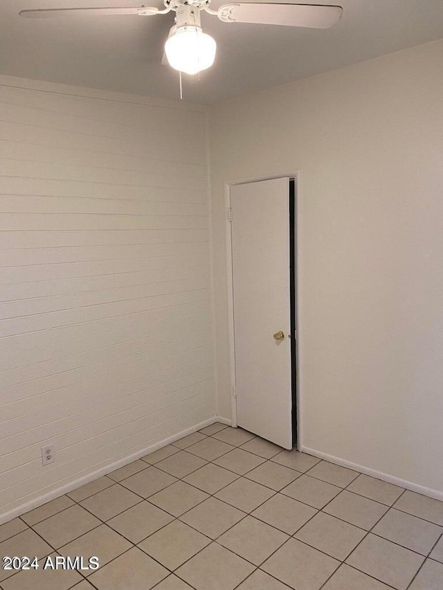 spare room featuring ceiling fan, light tile patterned floors, and brick wall