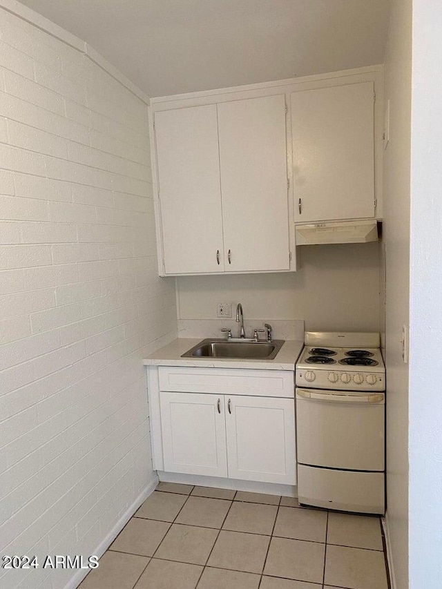 kitchen with sink, light tile patterned floors, brick wall, white range, and white cabinets