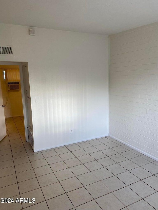 unfurnished room featuring brick wall, light tile patterned floors, and a wall unit AC