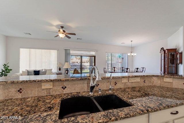 kitchen featuring pendant lighting, ceiling fan with notable chandelier, sink, and dark stone countertops