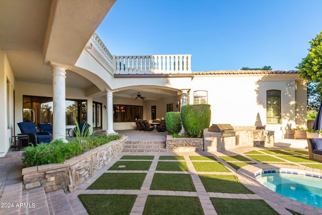 back of house with ceiling fan, a balcony, a patio area, exterior kitchen, and a hot tub