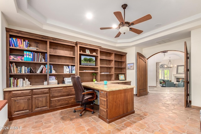 home office with ceiling fan with notable chandelier and a tray ceiling