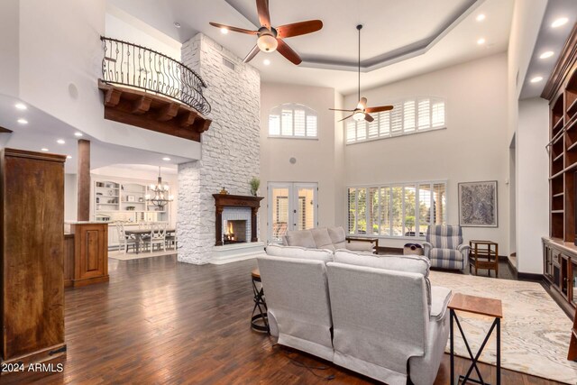 living room with ceiling fan, a high ceiling, a raised ceiling, built in features, and dark hardwood / wood-style floors