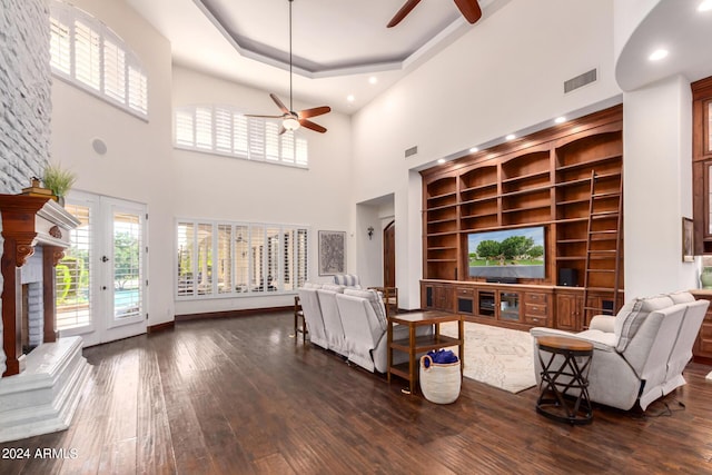 living room with ceiling fan, a high ceiling, a raised ceiling, dark hardwood / wood-style flooring, and built in features