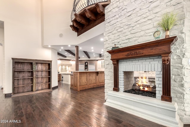 unfurnished living room with a multi sided fireplace, beamed ceiling, dark wood-type flooring, and a high ceiling