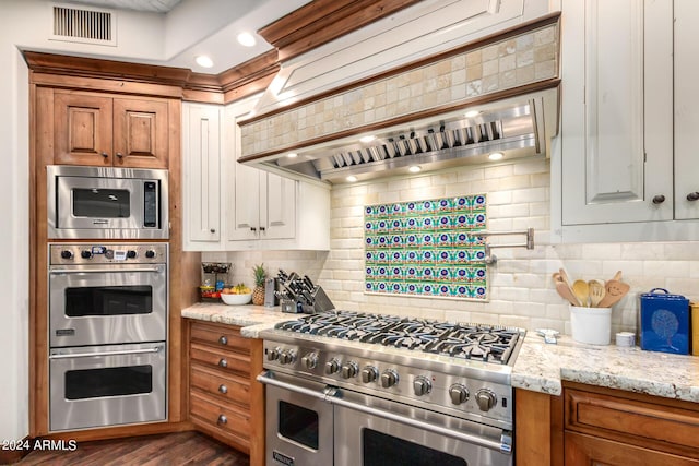 kitchen featuring appliances with stainless steel finishes, tasteful backsplash, light stone counters, custom range hood, and dark hardwood / wood-style floors