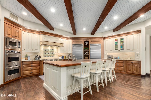 kitchen with butcher block counters, built in appliances, a spacious island, brick ceiling, and decorative backsplash