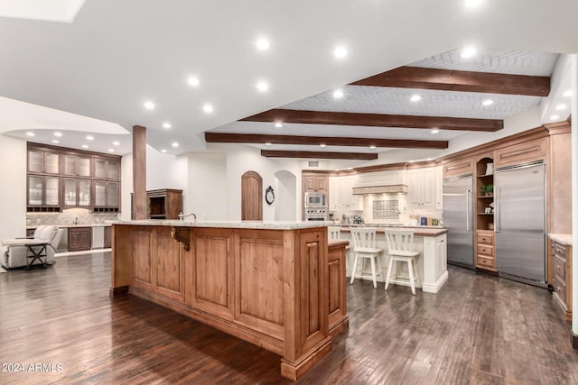 kitchen with built in appliances, a large island, a breakfast bar area, and tasteful backsplash