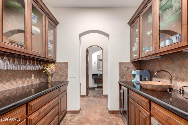 bar with decorative backsplash, sink, beverage cooler, and dark stone counters