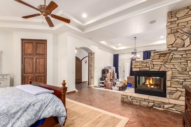 bedroom with ceiling fan with notable chandelier, a tray ceiling, and a stone fireplace