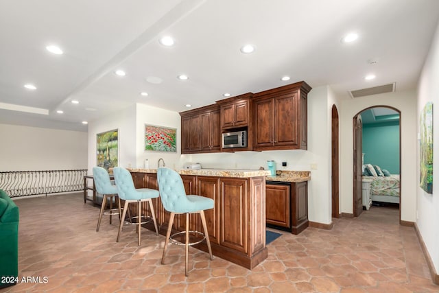 kitchen featuring light stone countertops, a kitchen bar, kitchen peninsula, and stainless steel microwave