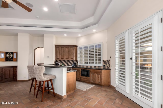 kitchen featuring kitchen peninsula, backsplash, black microwave, ceiling fan, and a breakfast bar area