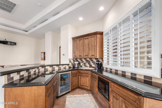 kitchen featuring dark stone counters, sink, kitchen peninsula, black microwave, and beverage cooler