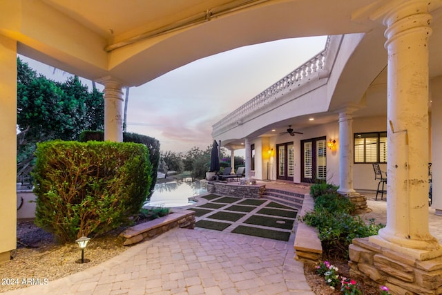 patio terrace at dusk featuring ceiling fan and a water view