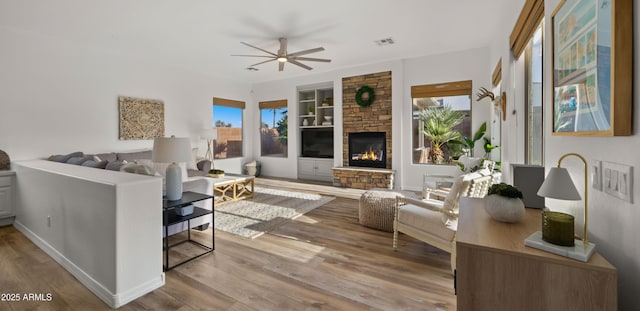 living room with a stone fireplace, a healthy amount of sunlight, built in shelves, and wood finished floors