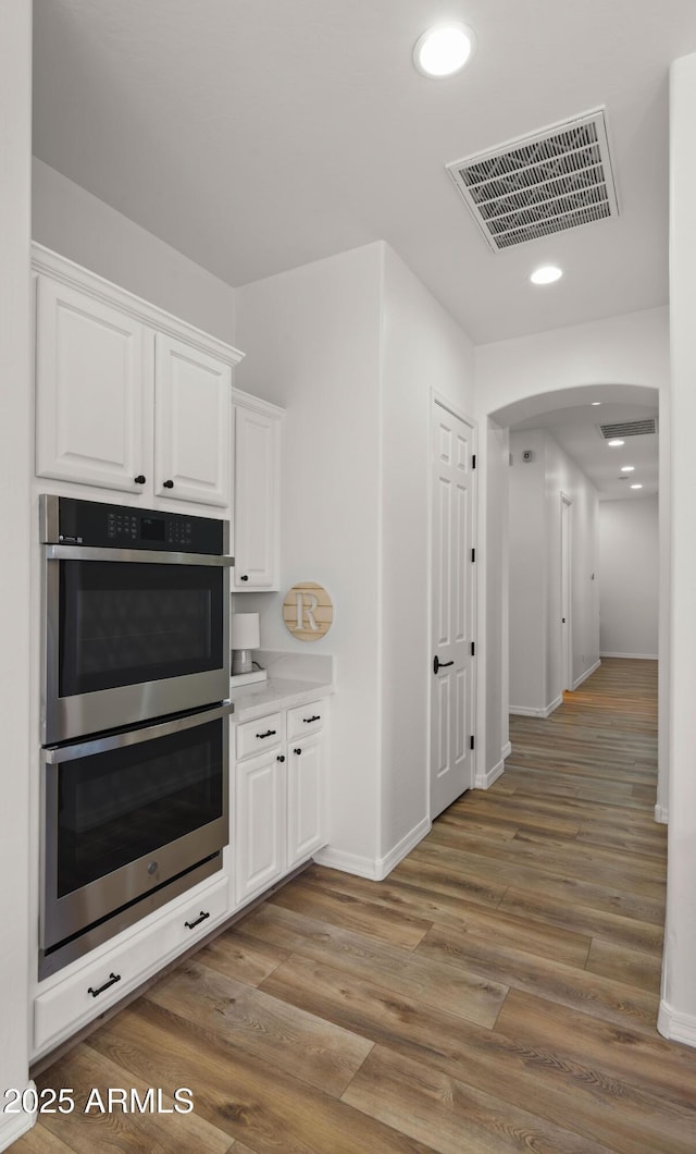 kitchen with wood finished floors, visible vents, stainless steel double oven, arched walkways, and white cabinets