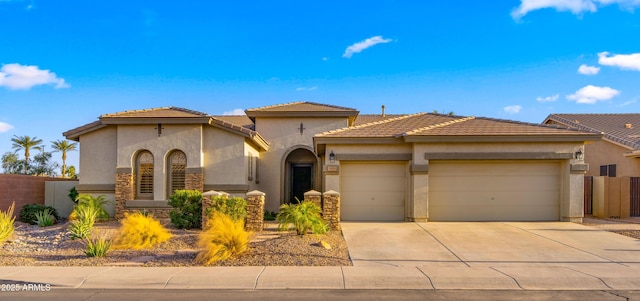 mediterranean / spanish-style house with fence, concrete driveway, stucco siding, a garage, and stone siding