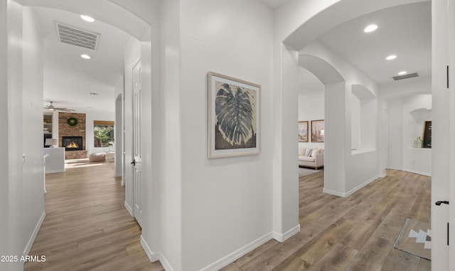 hall with visible vents, arched walkways, light wood-style floors, and baseboards