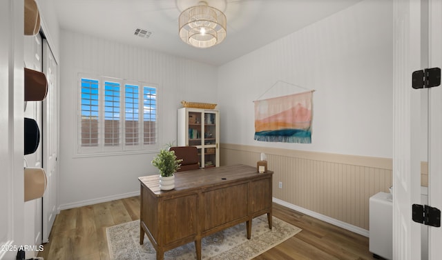 office area with visible vents, baseboards, a wainscoted wall, and wood finished floors