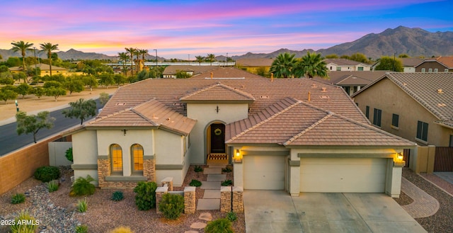 view of front facade featuring a tiled roof, concrete driveway, stucco siding, a garage, and a mountain view