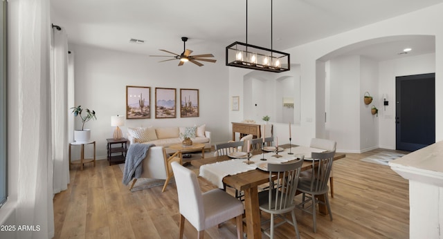 dining room featuring light wood-style floors, visible vents, arched walkways, and baseboards