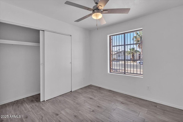 unfurnished bedroom featuring baseboards, a ceiling fan, a closet, and wood finished floors