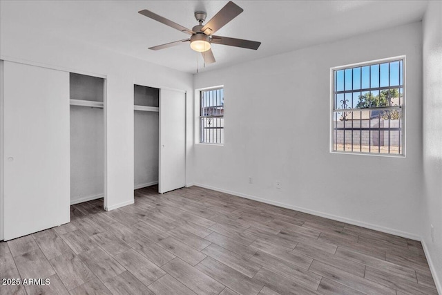 unfurnished bedroom featuring multiple closets, multiple windows, baseboards, and wood finished floors