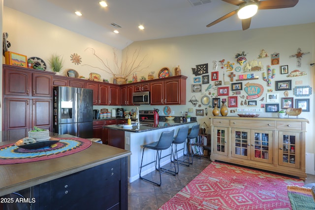 kitchen featuring appliances with stainless steel finishes, a kitchen bar, dark stone counters, ceiling fan, and kitchen peninsula