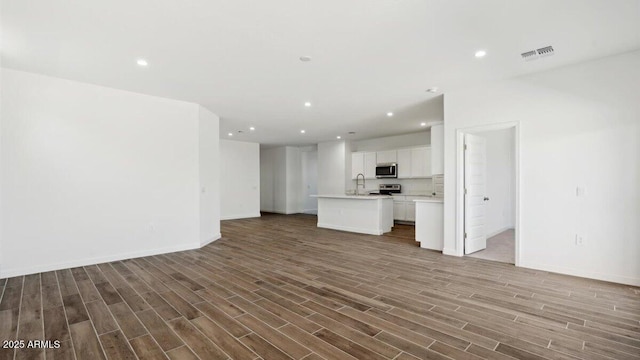 unfurnished living room featuring visible vents, baseboards, recessed lighting, wood finished floors, and a sink