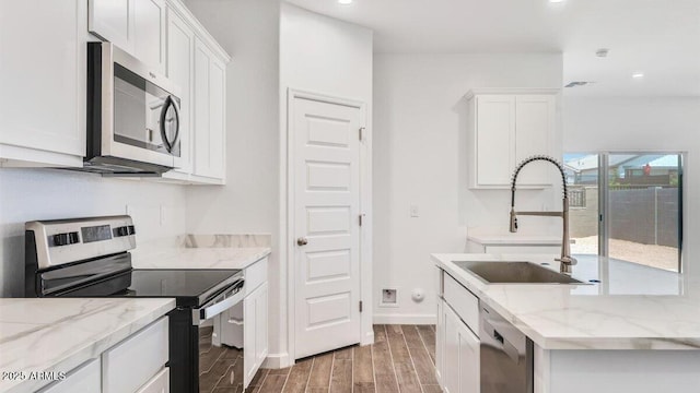 kitchen with a sink, stainless steel appliances, white cabinets, light stone countertops, and wood tiled floor