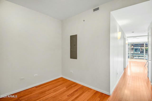 hallway with electric panel, light wood-style floors, visible vents, and baseboards