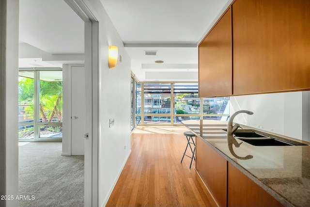 hall featuring visible vents, light wood-type flooring, baseboards, and a sink